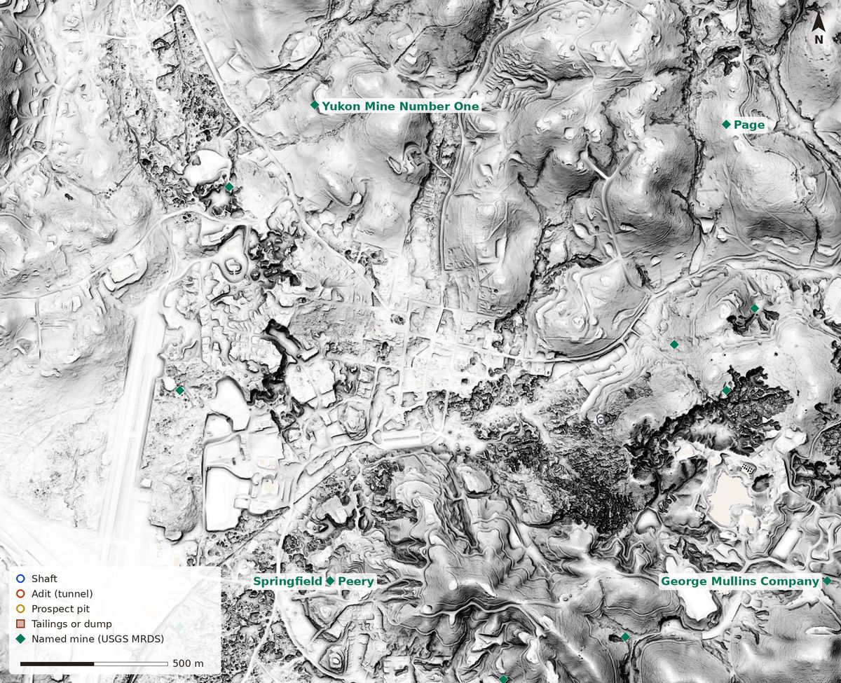 Bare-earth lidar relief of Columbia with mine markers: a pale grid of old town streets in the middle, a long flat airport runway on the left, and a band of rough, dark, pitted ground running south and east of town where limestone pinnacles were left by mining; green diamonds mark named mines