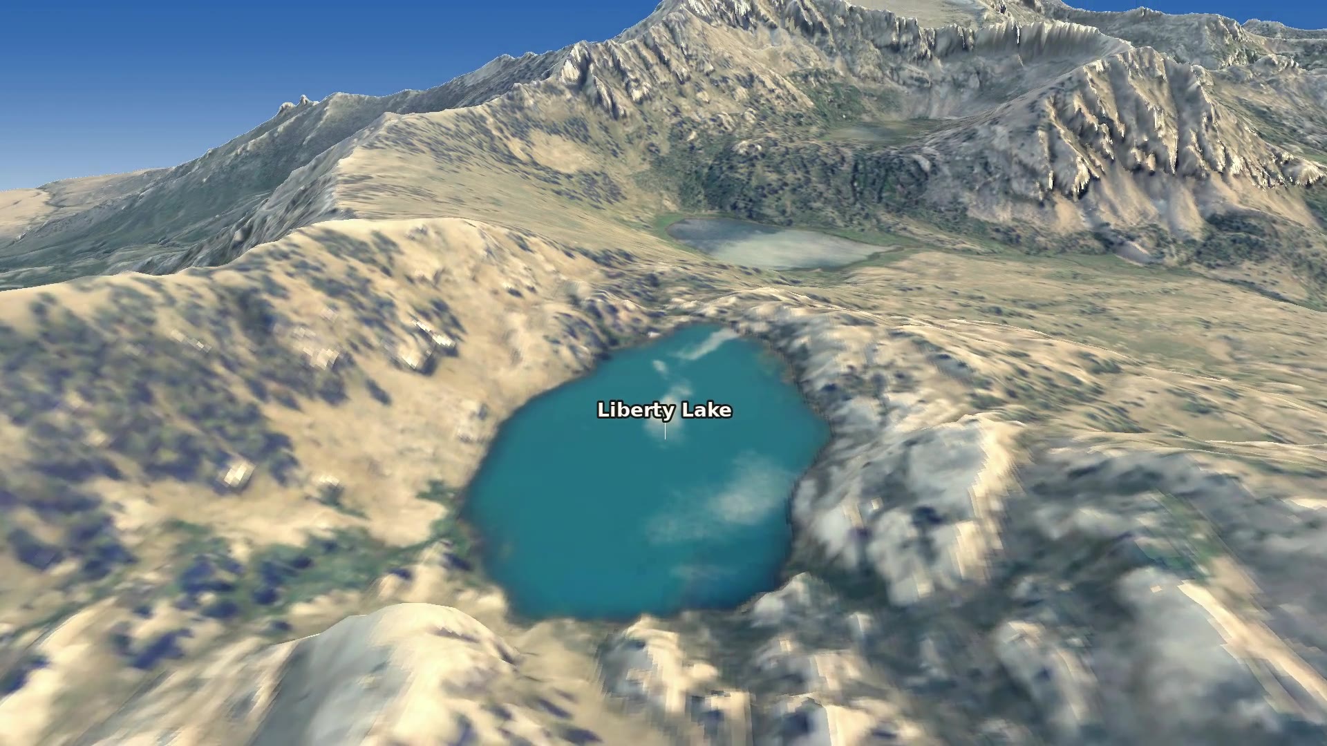 Looking down from Liberty Pass at Liberty Lake, deep blue in a rocky granite basin, with a smaller lake beyond and the crest of the Ruby Mountains running off to the south